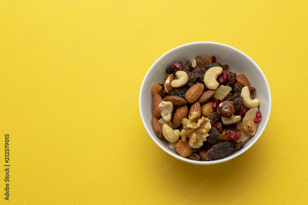 Mix of dried fruits and nuts in a bowl on a yellow background Mix of dried fruits and nuts in a bowl on a yellow background