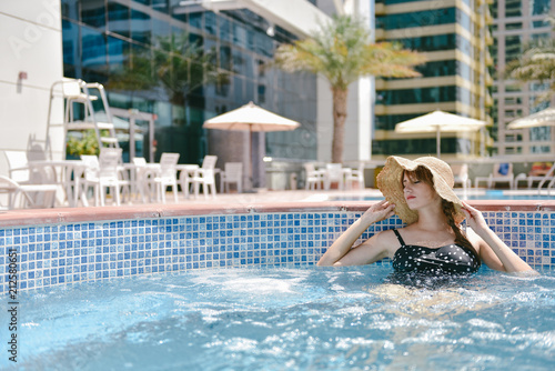 Beautiful young pregnant woman wearing swimsuit and hat relaxing in swimming pool © Tetiana