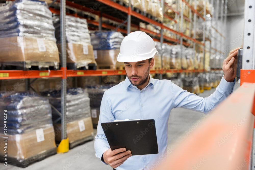 logistic business, shipment and people concept - businessman in helmet with clipboard checking goods at warehouse logistic business, shipment and people concept - businessman in helmet with clipboard checking goods at warehouse