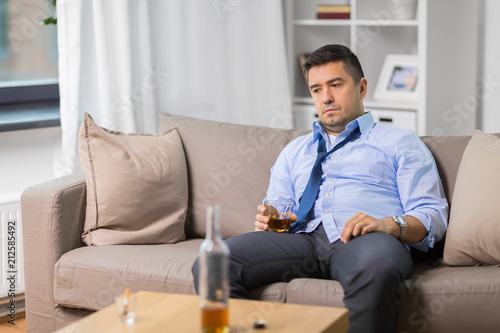 alcoholism, alcohol addiction and people concept - male alcoholic with glass drinking whiskey at home
