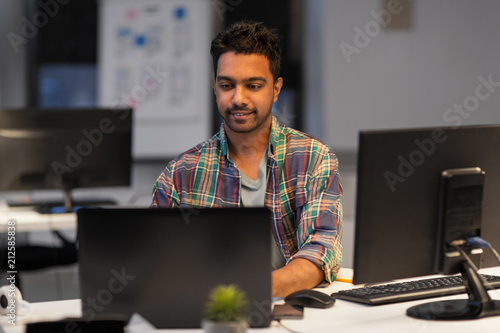 deadline, technology and people concept - creative man with laptop computer working at night office photo