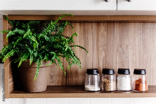 wooden shelf with pepper mill and spices and green plants on modern kitchen. cooking food. Stylish kitchen interior design in scandinavian style