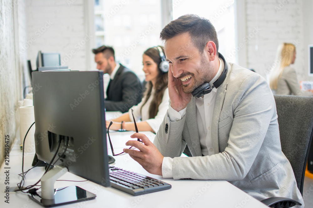 Happy business man with eyeglasses in hand looking at computer screen in office Happy business man with eyeglasses in hand looking at computer screen in office