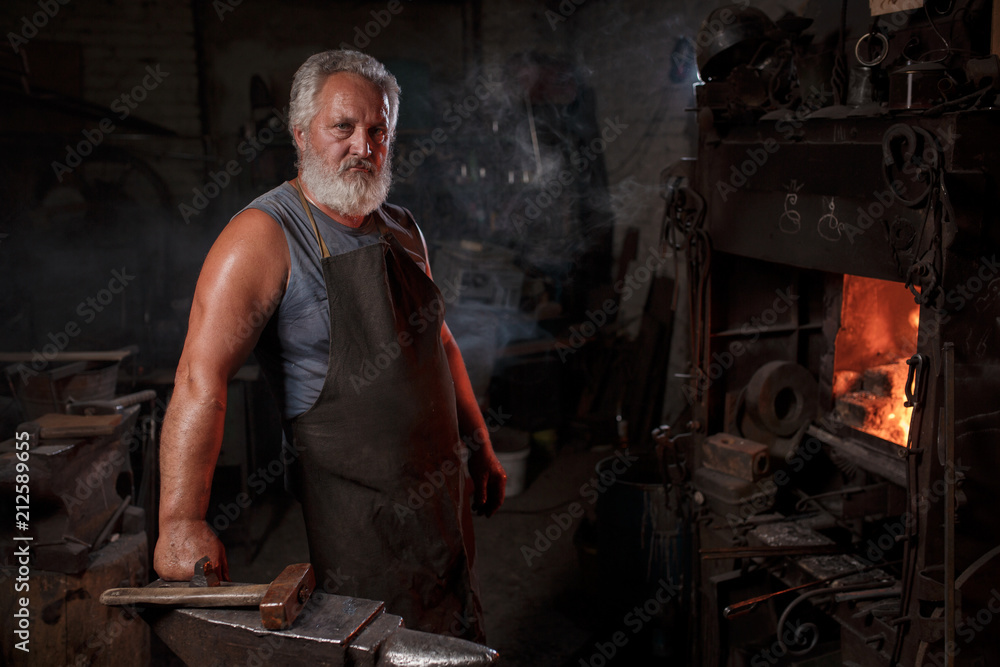 Portrait of a blacksmith artisan in an apron with an anvil in a blacksmith Portrait of a blacksmith artisan in an apron with an anvil in a blacksmith