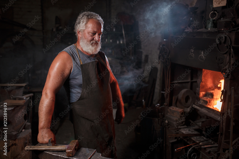 Portrait of a blacksmith artisan in an apron with an anvil in a blacksmith Portrait of a blacksmith artisan in an apron with an anvil in a blacksmith