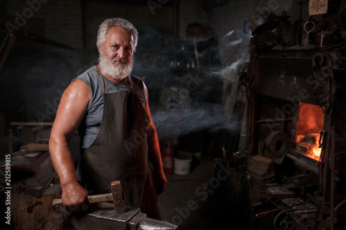 Portrait of a blacksmith artisan in an apron with an anvil in a blacksmith