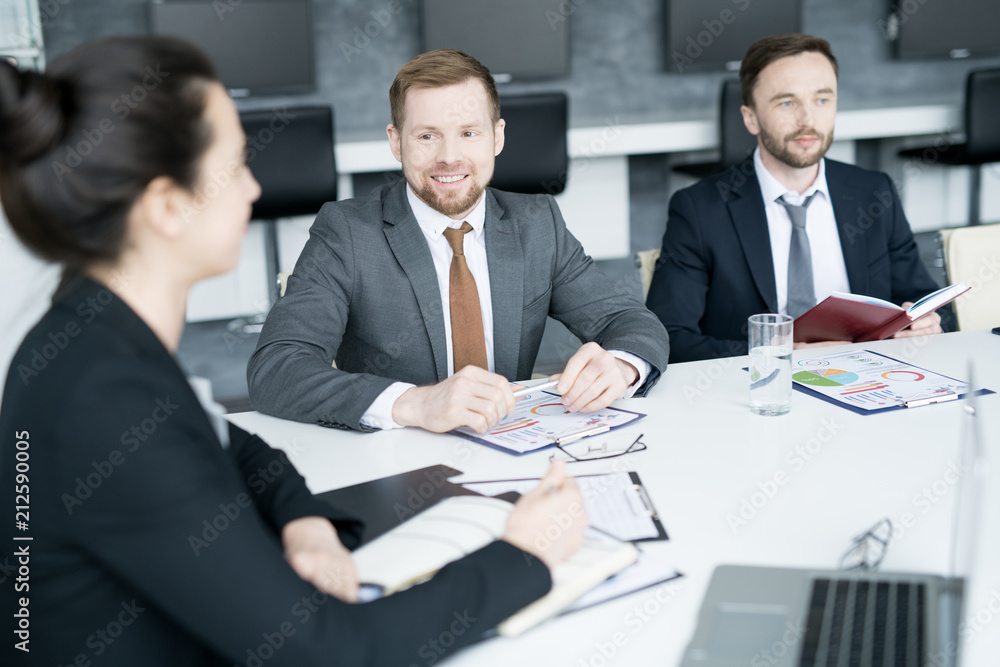 Group of three modern entrepreneurs sitting at meeting table in conference room and smiling while discussing startup project, copy space Group of three modern entrepreneurs sitting at meeting table in conference room and smiling while discussing startup project, copy space
