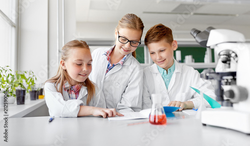 education, science and children concept - happy kids with workbooks studying chemistry at school laboratory