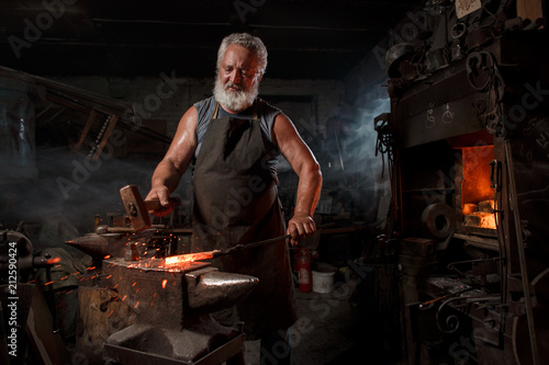 Billede på lærred Blacksmith with brush handles the molten metal