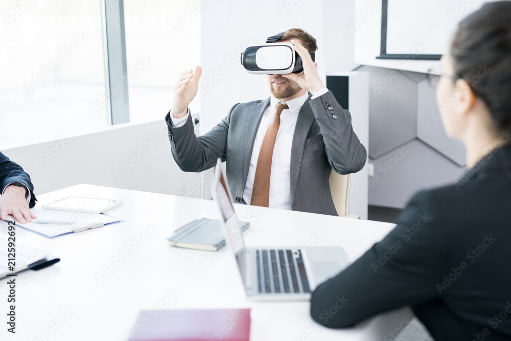 Fototapeta premium Portrait of contemporary businessman using VR while sitting at meeting table in conference room, copy space
