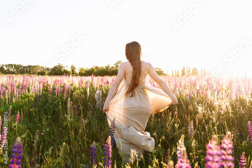 Young woman standing on a wildflower field with sunrise on the background