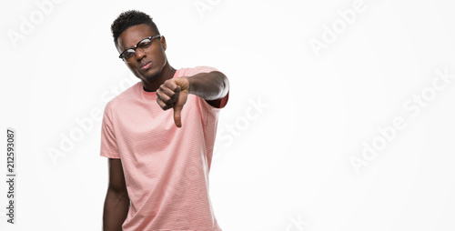 Young african american man wearing pink t-shirt looking unhappy and angry showing rejection and negative with thumbs down gesture. Bad expression.