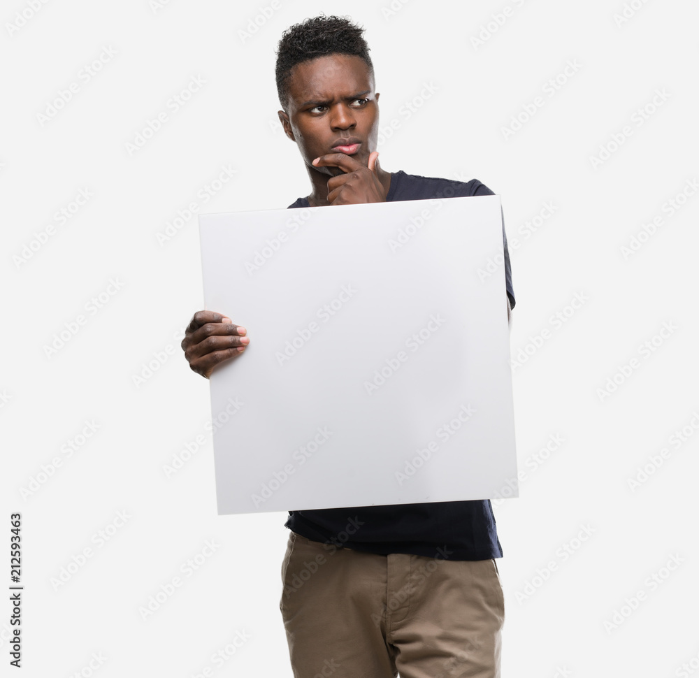 Young african american man holding a banner serious face thinking about question, very confused idea Young african american man holding a banner serious face thinking about question, very confused idea