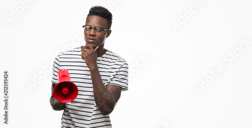 Young african american man holding megaphone serious face thinking about question, very confused idea