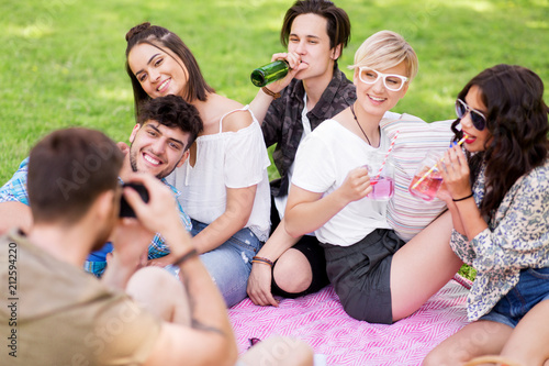 friendship, leisure and technology concept - group of happy smiling friends with non alcoholic drinks photographing at picnic in summer park © Syda Productions