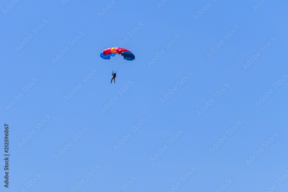 Parachutist descending with a parachute against blue sky Parachutist descending with a parachute against blue sky