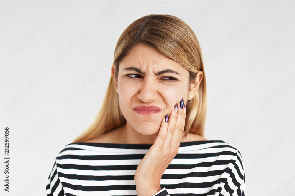 People, bad health condition and sickness concept. Studio shot of beautiful young Caucasian female having painful facial expression, pressing hand against her cheek while suffering from toothache People, bad health condition and sickness concept. Studio shot of beautiful young Caucasian female having painful facial expression, pressing hand against her cheek while suffering from toothache