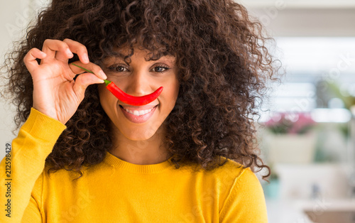 African american woman eating red hot chili pepper with a happy face standing and smiling with a confident smile showing teeth photo