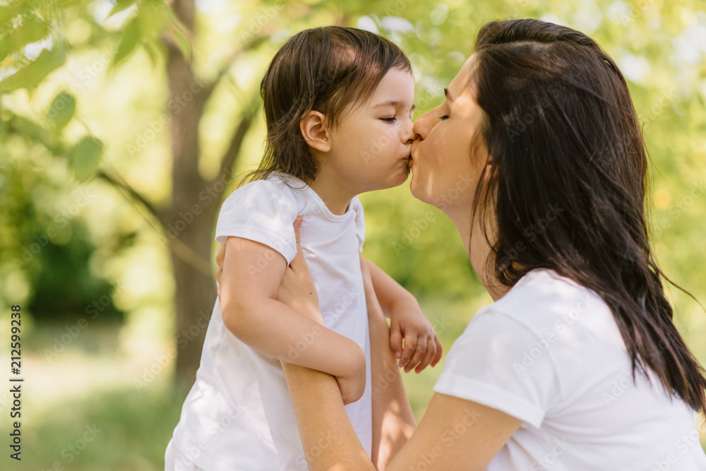 Portrait of Caucasian beautiful mother and her cute kid playing outdoors, holding each other and give a kiss. Pretty woman and her child girl enjoy the time together in the park. People, motherhood Portrait of Caucasian beautiful mother and her cute kid playing outdoors, holding each other and give a kiss. Pretty woman and her child girl enjoy the time together in the park. People, motherhood