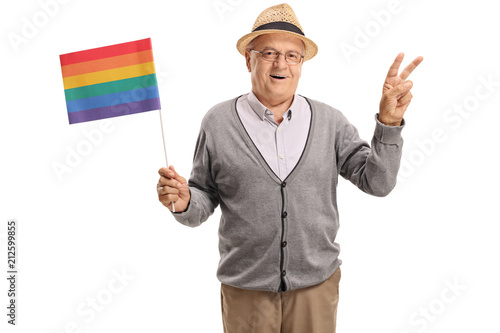 Fototapeta Mature man holding a rainbow flag and making a peace gesture