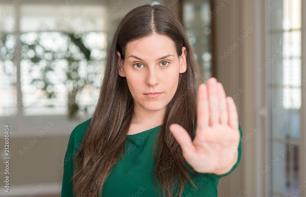 Young beautiful woman at home with open hand doing stop sign with serious and confident expression, defense gesture Young beautiful woman at home with open hand doing stop sign with serious and confident expression, defense gesture