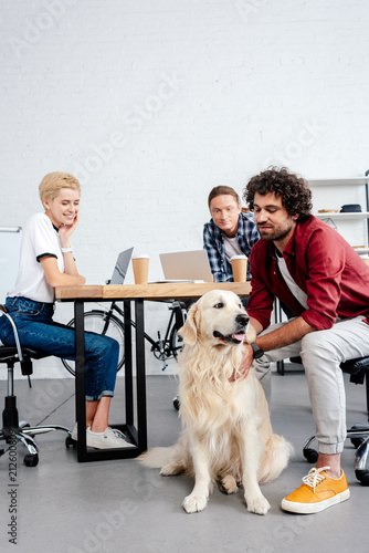 smiling young business colleagues looking at dog while working in office