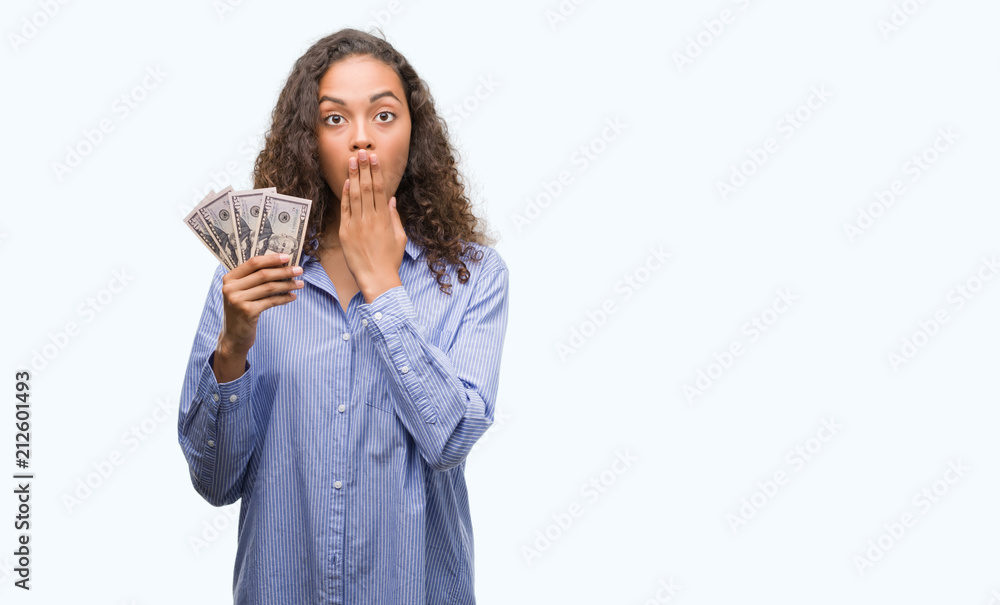 Young hispanic woman holding dollars cover mouth with hand shocked with shame for mistake, expression of fear, scared in silence, secret concept Young hispanic woman holding dollars cover mouth with hand shocked with shame for mistake, expression of fear, scared in silence, secret concept