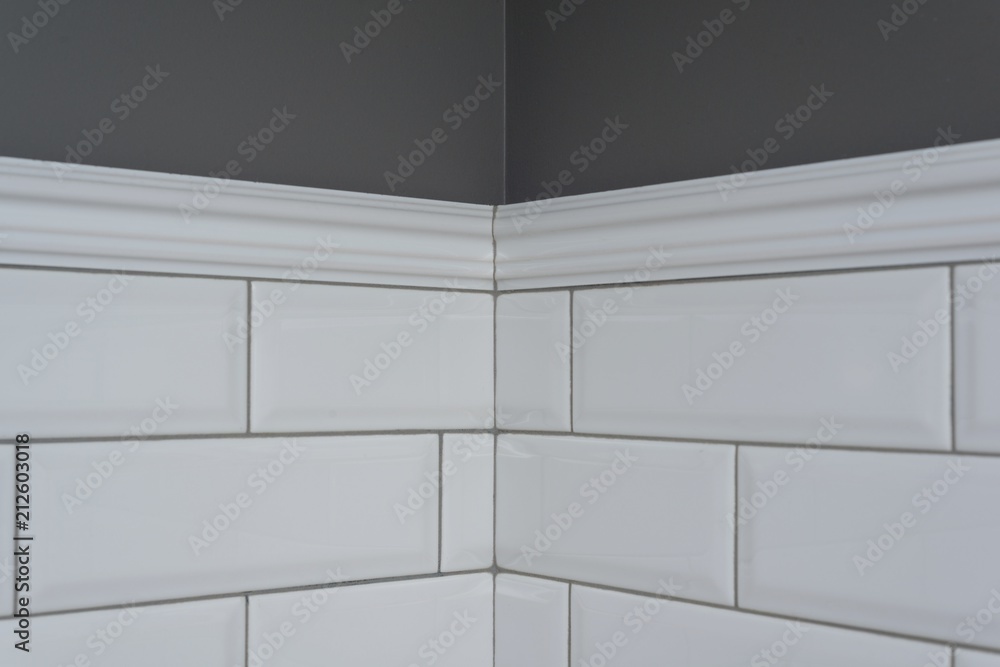 Gray painted wall, part of the wall is covered tiles small white glossy  brick, ceramic decorative molding tiles, detail of intricate corner.  Fragment of the walls of the bathroom, toilet, kitchen. Stock-Foto