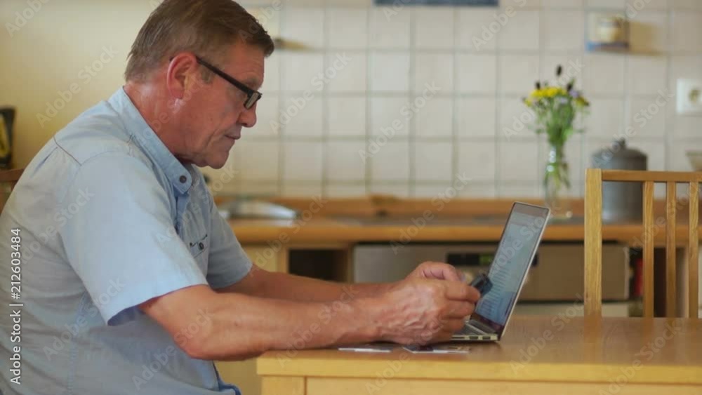 An elderly man works with a computer and phone, sitting at a table in his kitchen. Glasses for vision and protection An elderly man works with a computer and phone, sitting at a table in his kitchen. Glasses for vision and protection