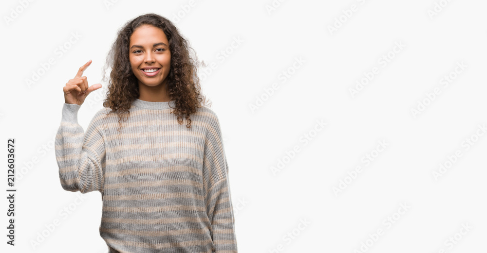 Beautiful young hispanic woman wearing stripes sweater smiling and confident gesturing with hand doing size sign with fingers while looking and the camera. Measure concept. Beautiful young hispanic woman wearing stripes sweater smiling and confident gesturing with hand doing size sign with fingers while looking and the camera. Measure concept.