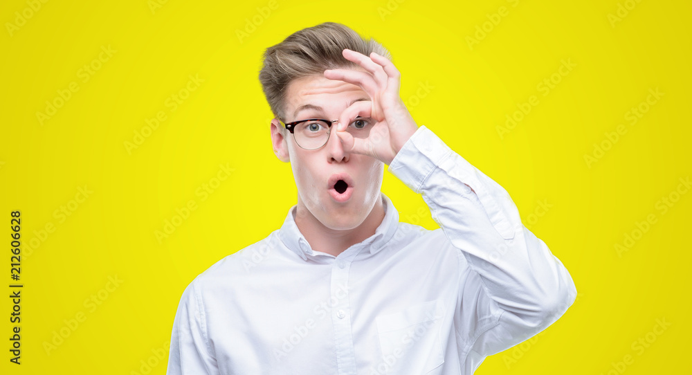 Young handsome blond man doing ok gesture shocked with surprised face, eye looking through fingers. Unbelieving expression. Young handsome blond man doing ok gesture shocked with surprised face, eye looking through fingers. Unbelieving expression.