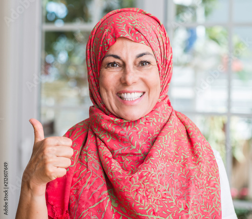Middle aged muslim woman wearing hijab pointing with hand and finger up with happy face smiling