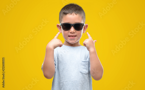 Dark haired little child wearing sunglasses very happy pointing with hand and finger © Krakenimages.com