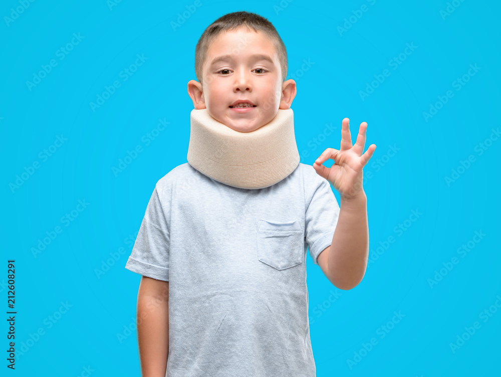 Dark haired little child injured wearing neck collar doing ok sign with fingers, excellent symbol Dark haired little child injured wearing neck collar doing ok sign with fingers, excellent symbol