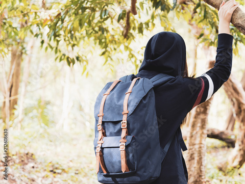 photographer and adventure in nature concept from beauty long hair asian woman in warm suit and backpack hold the tree for relax in tropical forest