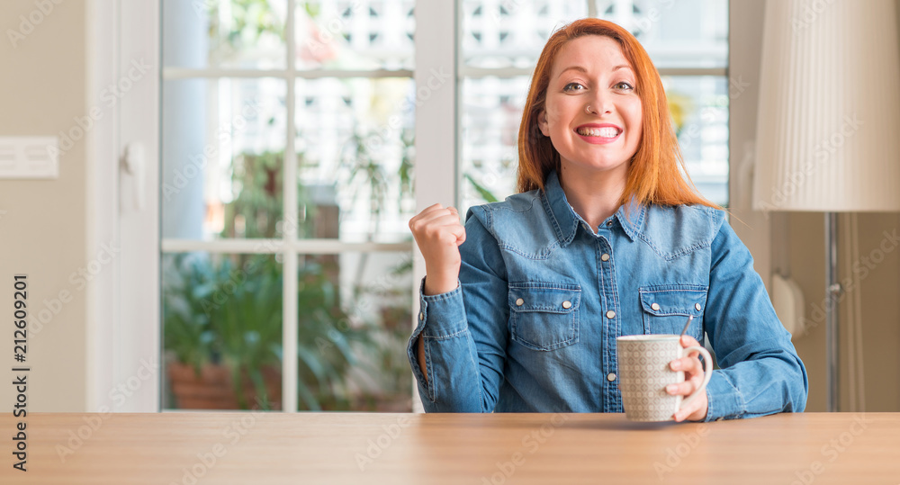 Fototapeta premium Redhead woman holding a cup of coffee screaming proud and celebrating victory and success very excited, cheering emotion