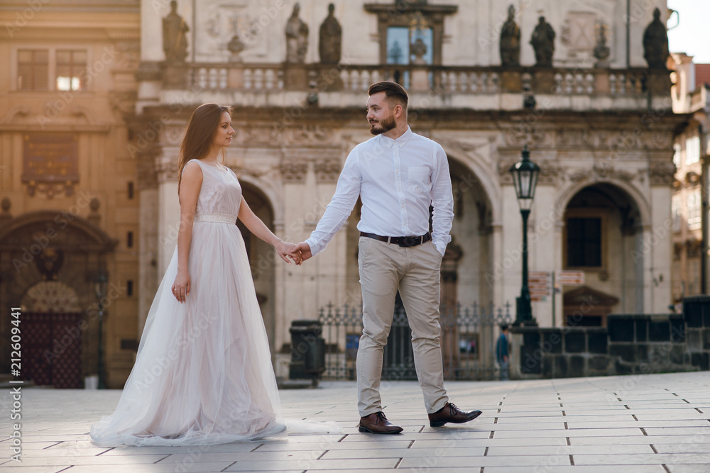 Romantic wedding couple of groom and bride in gorgeous dress holding hands while walking the old street of Prague. Czech Republic