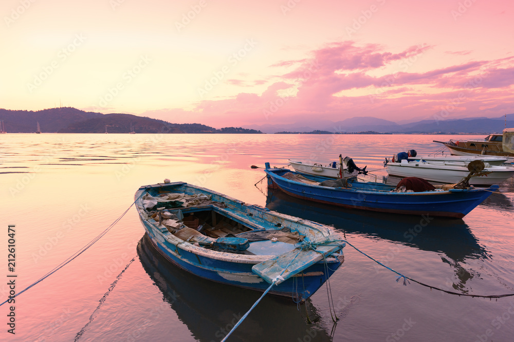 Old boats in the port. Colorful sunrise or sunset, clouds and mountains on the horizon