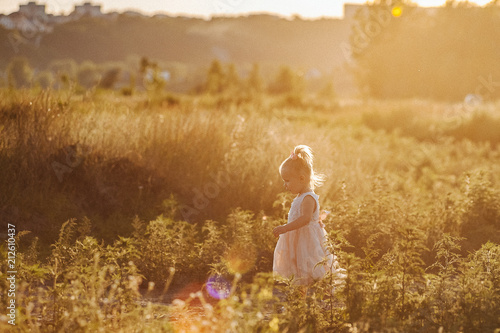 A girl walks in nature in the rays of the setting sun. Children's family vacation. Baby is dressed in a beautiful dress. One-year-old child