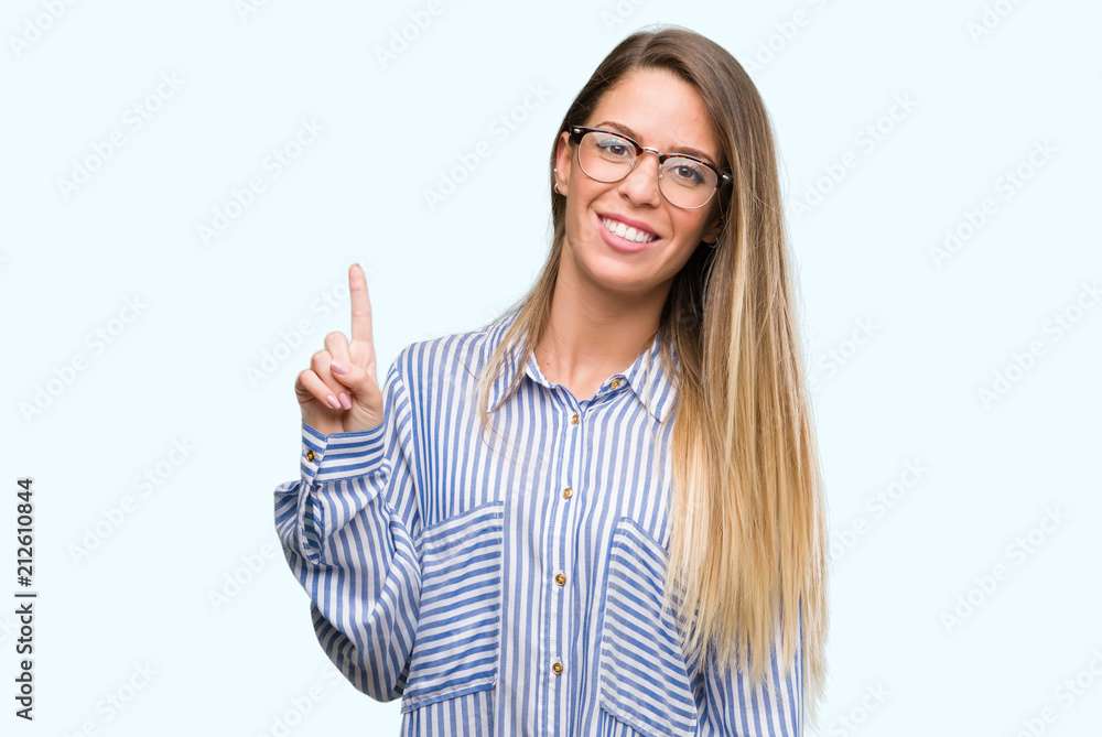 Beautiful young woman wearing elegant shirt and glasses showing and pointing up with finger number one while smiling confident and happy. Beautiful young woman wearing elegant shirt and glasses showing and pointing up with finger number one while smiling confident and happy.