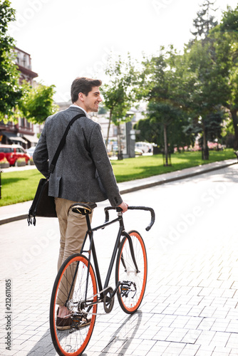 Fototapeta Naklejka Na Ścianę i Meble -  Back view of young businessman walking with a bicycle