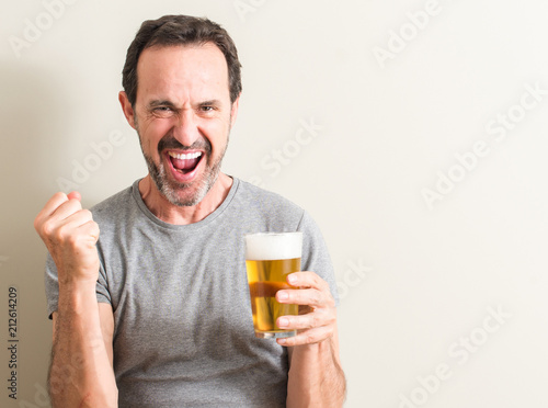 Senior man drinking beer screaming proud and celebrating victory and success very excited, cheering emotion