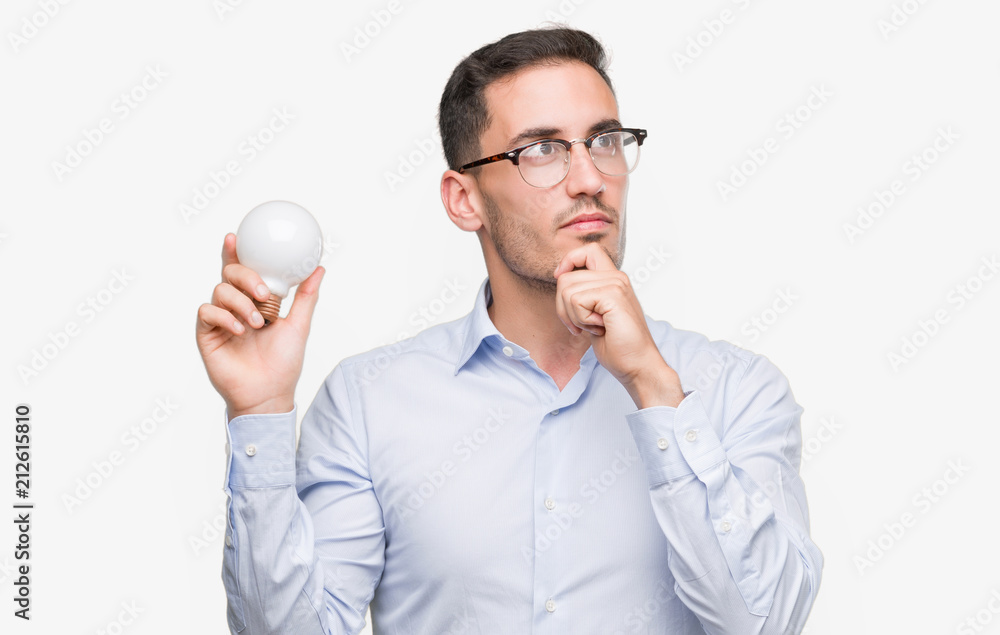 Handsome young man holding lightbulb as idea serious face thinking about question, very confused idea Handsome young man holding lightbulb as idea serious face thinking about question, very confused idea