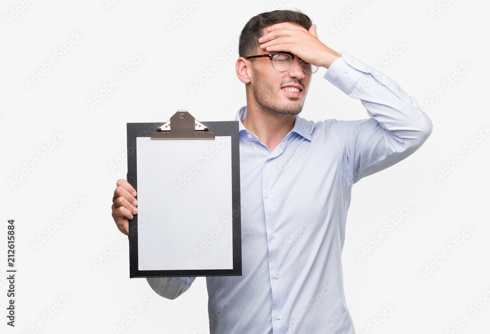 Handsome young business man showing a clipboard stressed with hand on head, shocked with shame and surprise face, angry and frustrated. Fear and upset for mistake. Handsome young business man showing a clipboard stressed with hand on head, shocked with shame and surprise face, angry and frustrated. Fear and upset for mistake.