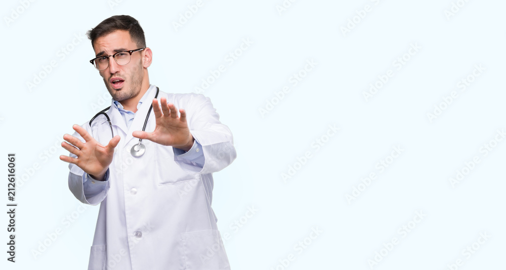 Handsome young doctor man afraid and terrified with fear expression stop gesture with hands, shouting in shock. Panic concept. Handsome young doctor man afraid and terrified with fear expression stop gesture with hands, shouting in shock. Panic concept.