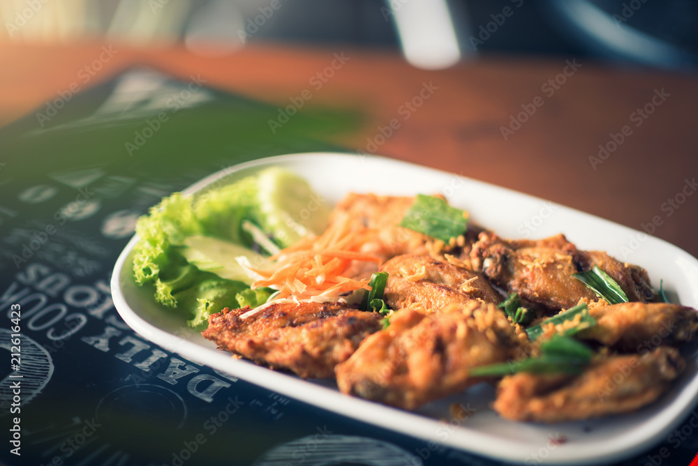 Thai style fried chicken wings on a round white plate on a wood table Thai style fried chicken wings on a round white plate on a wood table