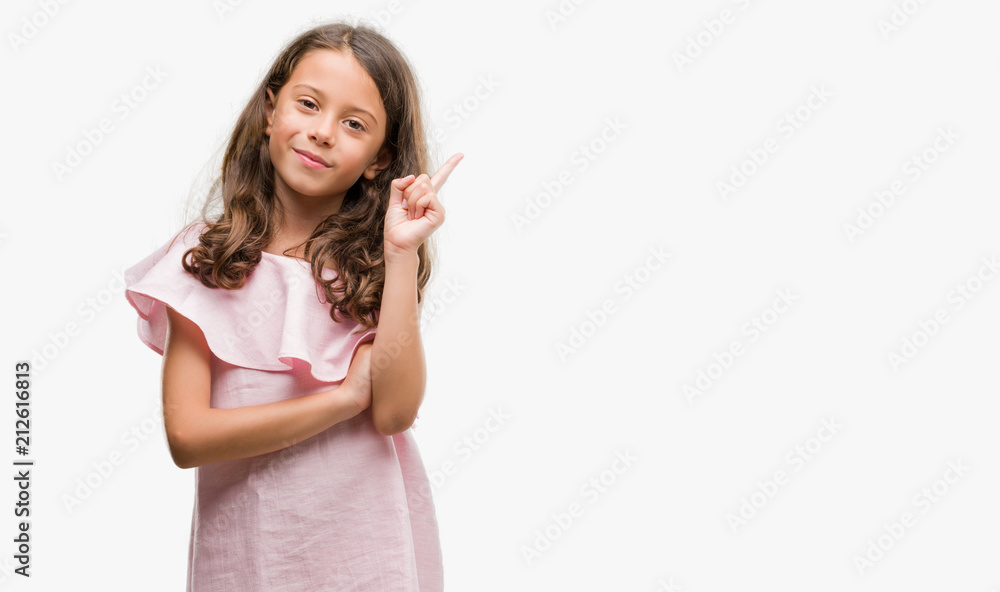 Brunette hispanic girl wearing pink dress with a big smile on face, pointing with hand and finger to the side looking at the camera. Brunette hispanic girl wearing pink dress with a big smile on face, pointing with hand and finger to the side looking at the camera.