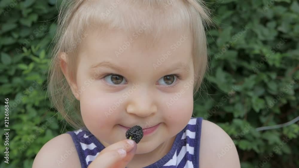 A cute little girl eats fresh mulberry with pleasure A cute little girl eats fresh mulberry with pleasure