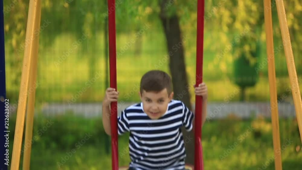 A little boy in a striped T-shirt is playing on the playground, Swing on a swing.Spring, sunny weather A little boy in a striped T-shirt is playing on the playground, Swing on a swing.Spring, sunny weather