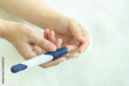 Close up of woman hands using lancet on finger to check blood sugar level by Glucose meter on bed in the morning. Medicine  diabetes  glycemia  health care concept.